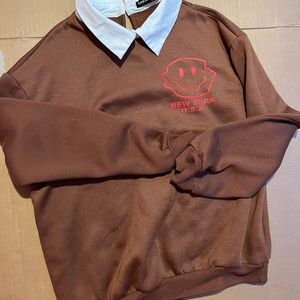 Brown white collared crewneck with a red smiley face and red letter